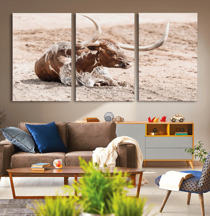 Texas Longhorn bull resting on dusty ground with warm tones, ideal for rustic western or farmhouse-themed wall decor.