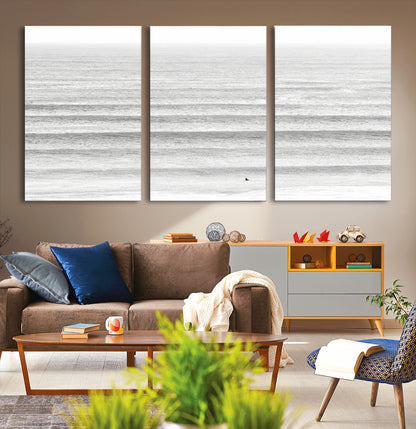 Monochrome photo of a lone surfer in calm layered waves, perfect for minimalist coastal or moody ocean-inspired wall decoration.