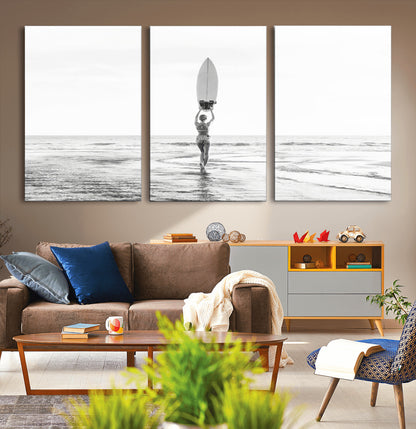 Black and white image of a female surfer holding a surfboard above her head while walking toward the ocean, creating a minimalist and bold coastal aesthetic.
