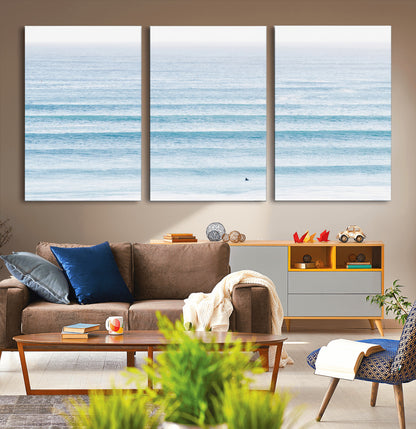 Minimalist ocean view with soft blue waves and a lone surfer, creating a serene and airy coastal aesthetic, perfect for tranquil home decor.
