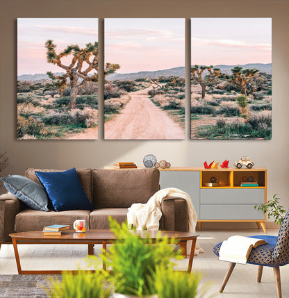 A dusty road winding through Joshua Tree National Park, framed by iconic twisted trees and warm desert tones under a soft pastel sky.