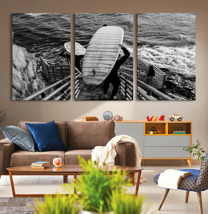 Black and white photo of surfers carrying boards down a rugged cliffside stairway, capturing a bold and adventurous coastal scene.