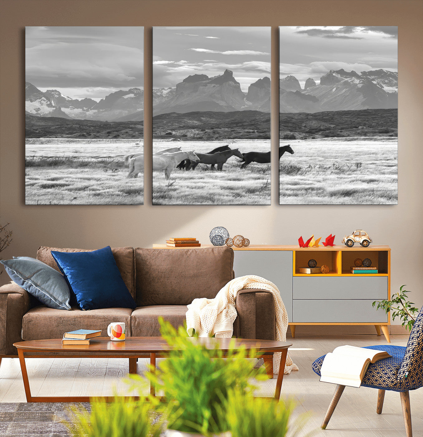 A black and white landscape of wild horses grazing in a vast grassland with towering mountains in the background, creating a moody and rustic western aesthetic.