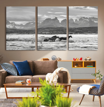 A black and white landscape of wild horses grazing in a vast grassland with towering mountains in the background, creating a moody and rustic western aesthetic.