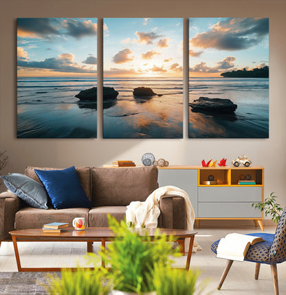 A serene beach at sunset with vibrant clouds, calm water, and rocks in the foreground reflecting the warm colors of the setting sun.