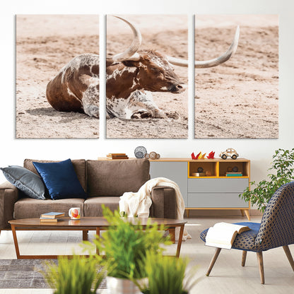 Texas Longhorn bull resting on dusty ground with warm tones, ideal for rustic western or farmhouse-themed wall decor.