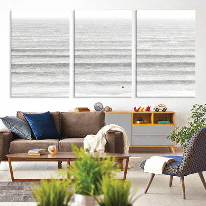 Monochrome photo of a lone surfer in calm layered waves, perfect for minimalist coastal or moody ocean-inspired wall decoration.