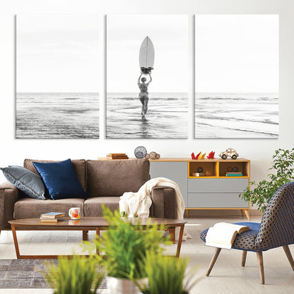Black and white image of a female surfer holding a surfboard above her head while walking toward the ocean, creating a minimalist and bold coastal aesthetic.