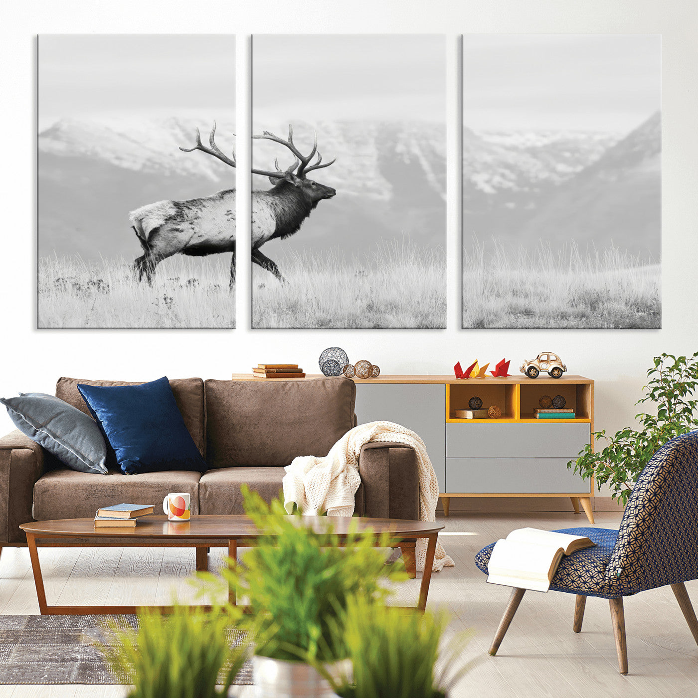 Black and white photograph of a majestic elk standing in a grassy field with snow-capped mountains in the background, creating a bold and rustic wilderness scene.