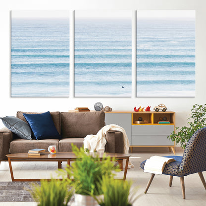 Minimalist ocean view with soft blue waves and a lone surfer, creating a serene and airy coastal aesthetic, perfect for tranquil home decor.