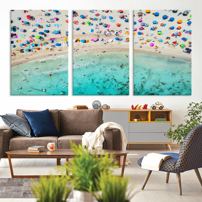Aerial view of a vibrant beach filled with colorful umbrellas and people enjoying the turquoise ocean, capturing a lively summer vacation scene.