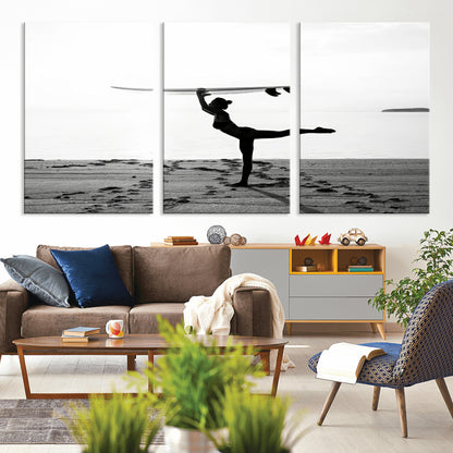 A woman balances a surfboard on her head while striking a yoga pose on the beach, silhouetted against a calm ocean horizon.