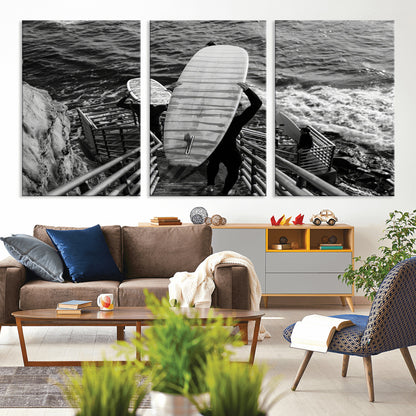Black and white photo of surfers carrying boards down a rugged cliffside stairway, capturing a bold and adventurous coastal scene.