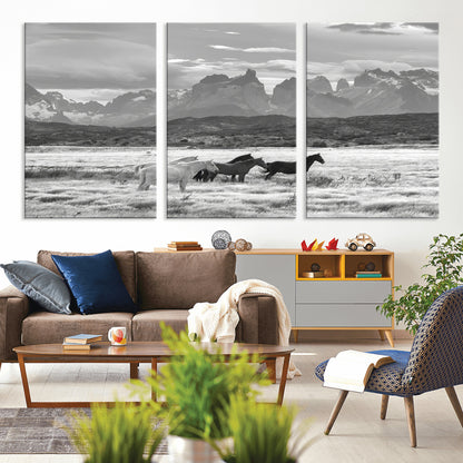 A black and white landscape of wild horses grazing in a vast grassland with towering mountains in the background, creating a moody and rustic western aesthetic.