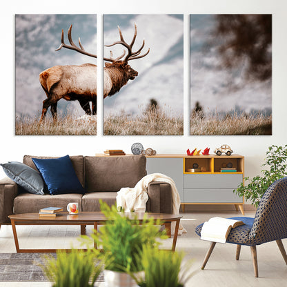 Majestic elk with large antlers standing in grass with snowy mountains in background, perfect for rustic cabin or lodge style decor.